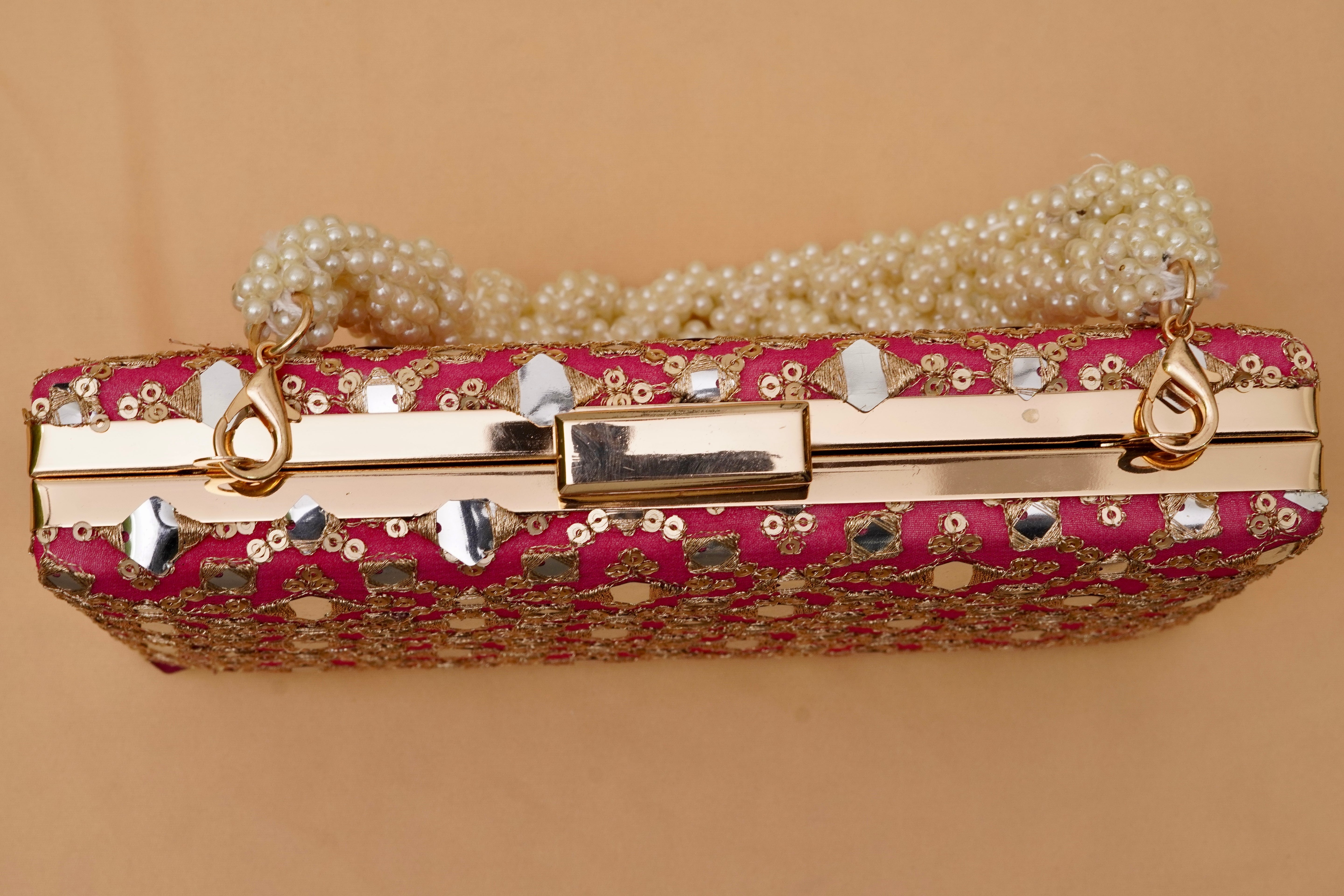 Pink clutch with gold accents and pearl chain on a beige background